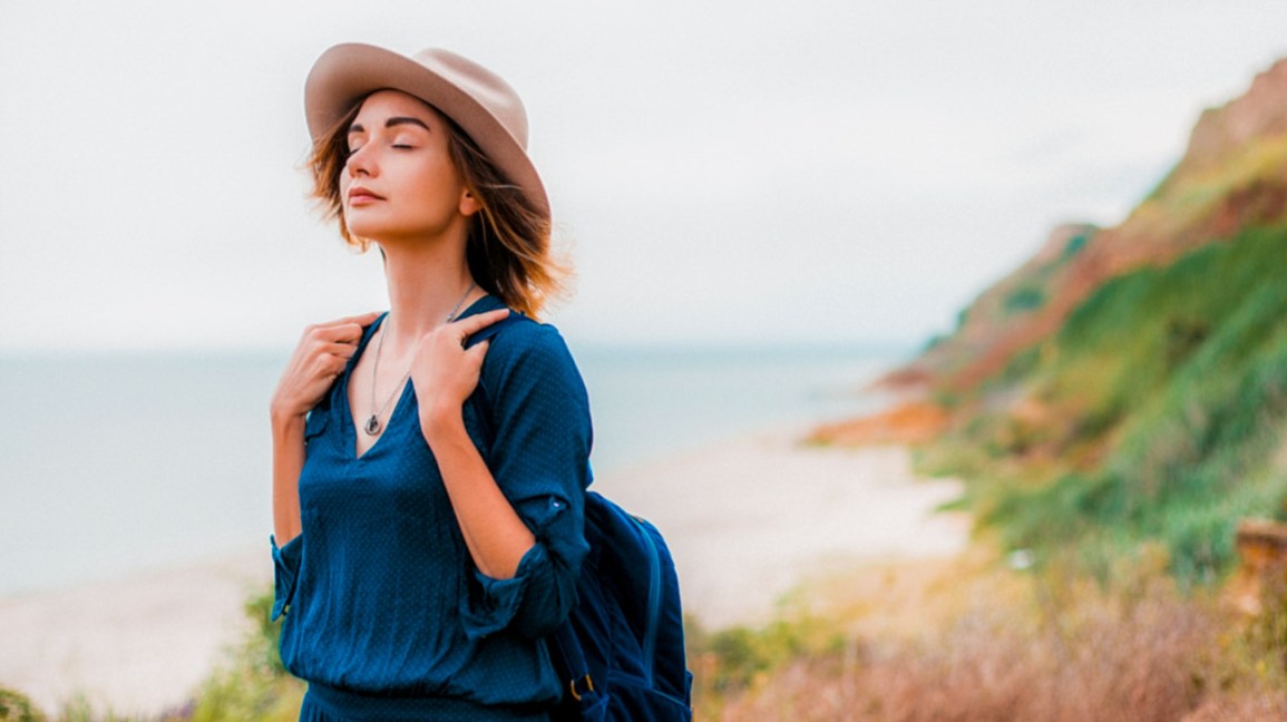 Mid adult woman in coastal setting, carrying backpack, breathing in fresh air